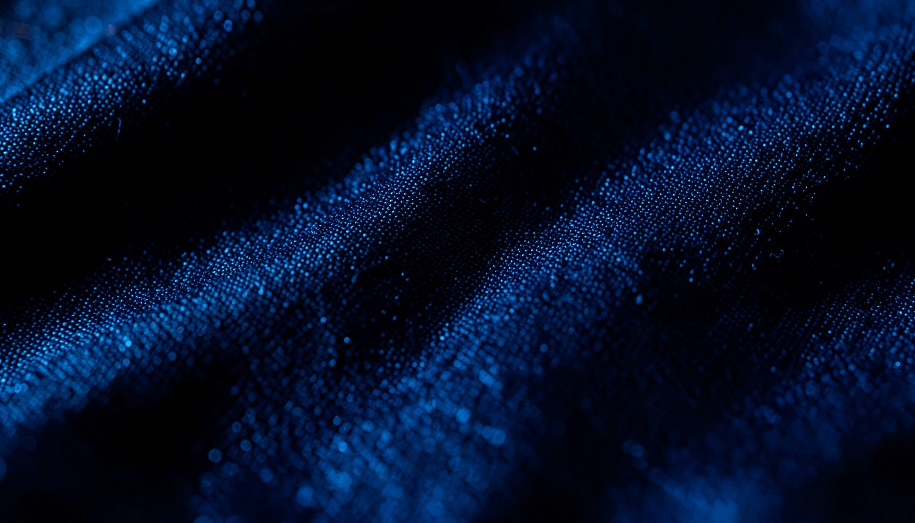 Extreme close-up of dark navy fabric with a subtle metallic sheen, fine woven texture catching low light