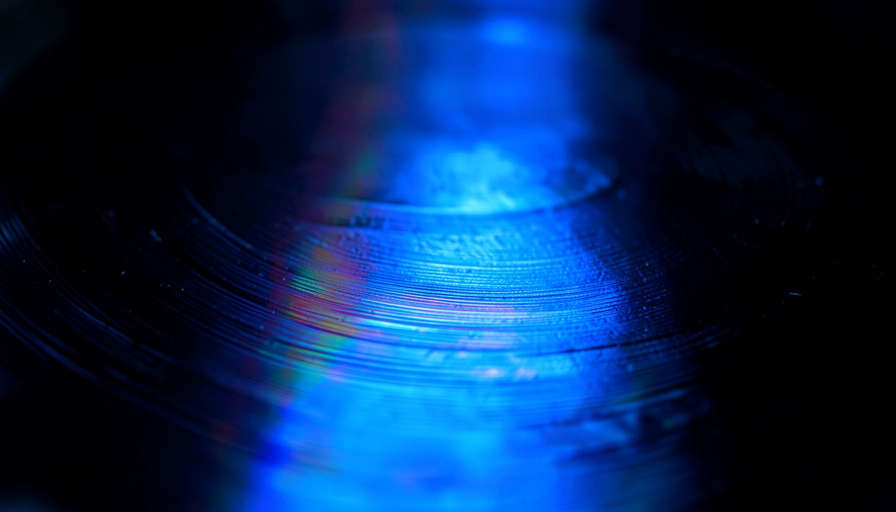 Extreme close-up of glossy vinyl record surface with subtle rainbow reflections and fine groove texture against deep black