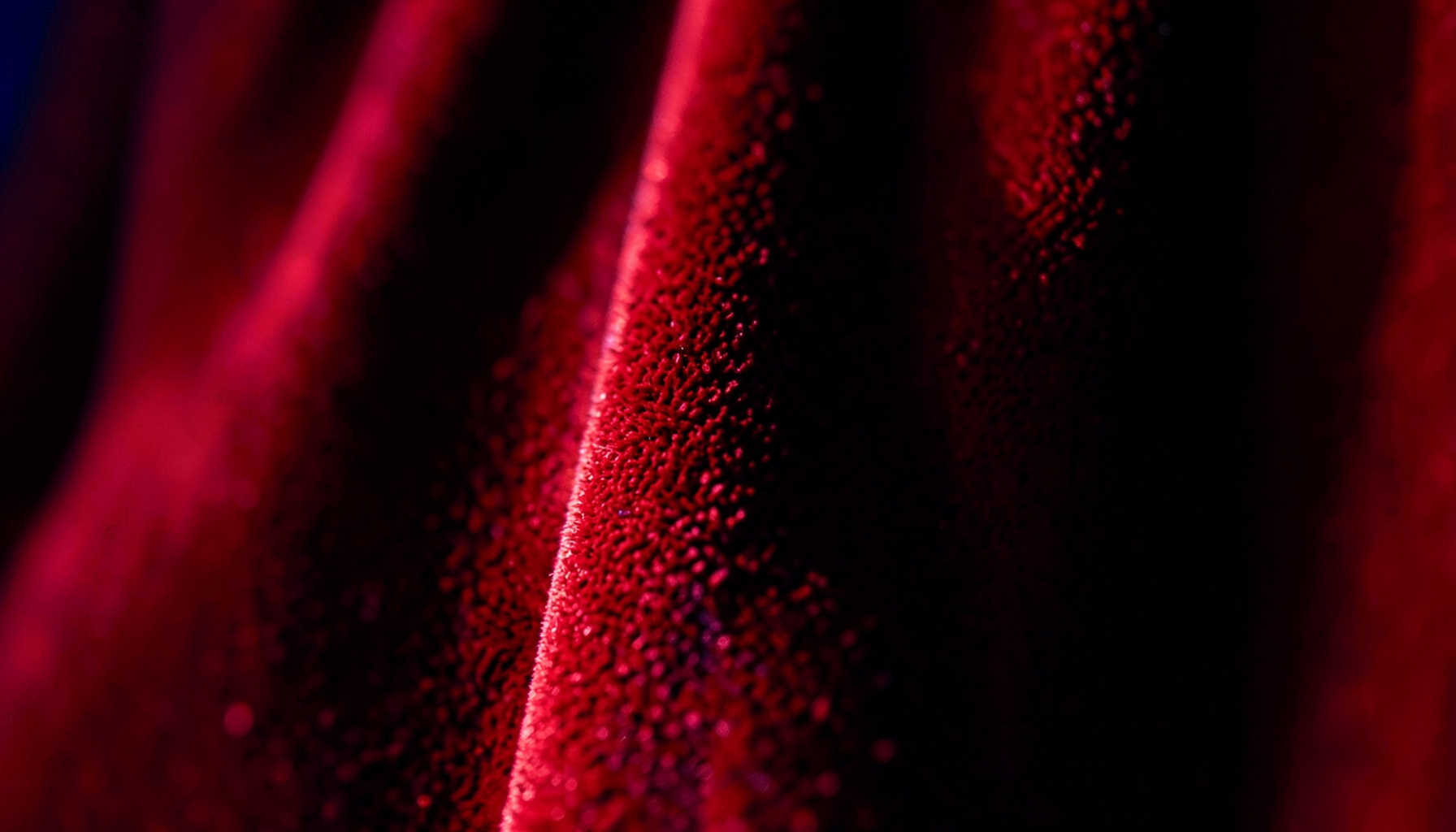 Close-up of rich red velvet theater curtains with dramatic stage lighting casting deep shadows and warm highlights